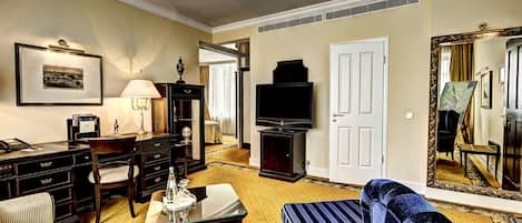 A hotel room with a sofa, a table, a lamp, a television, and a mirror.