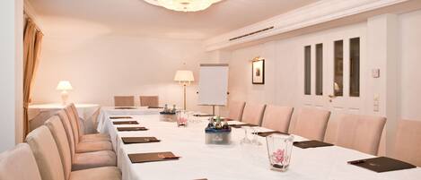 Ein Konferenzraum mit langem Tisch, Stühlen, einer Kristallleuchtre und einer Tafel.