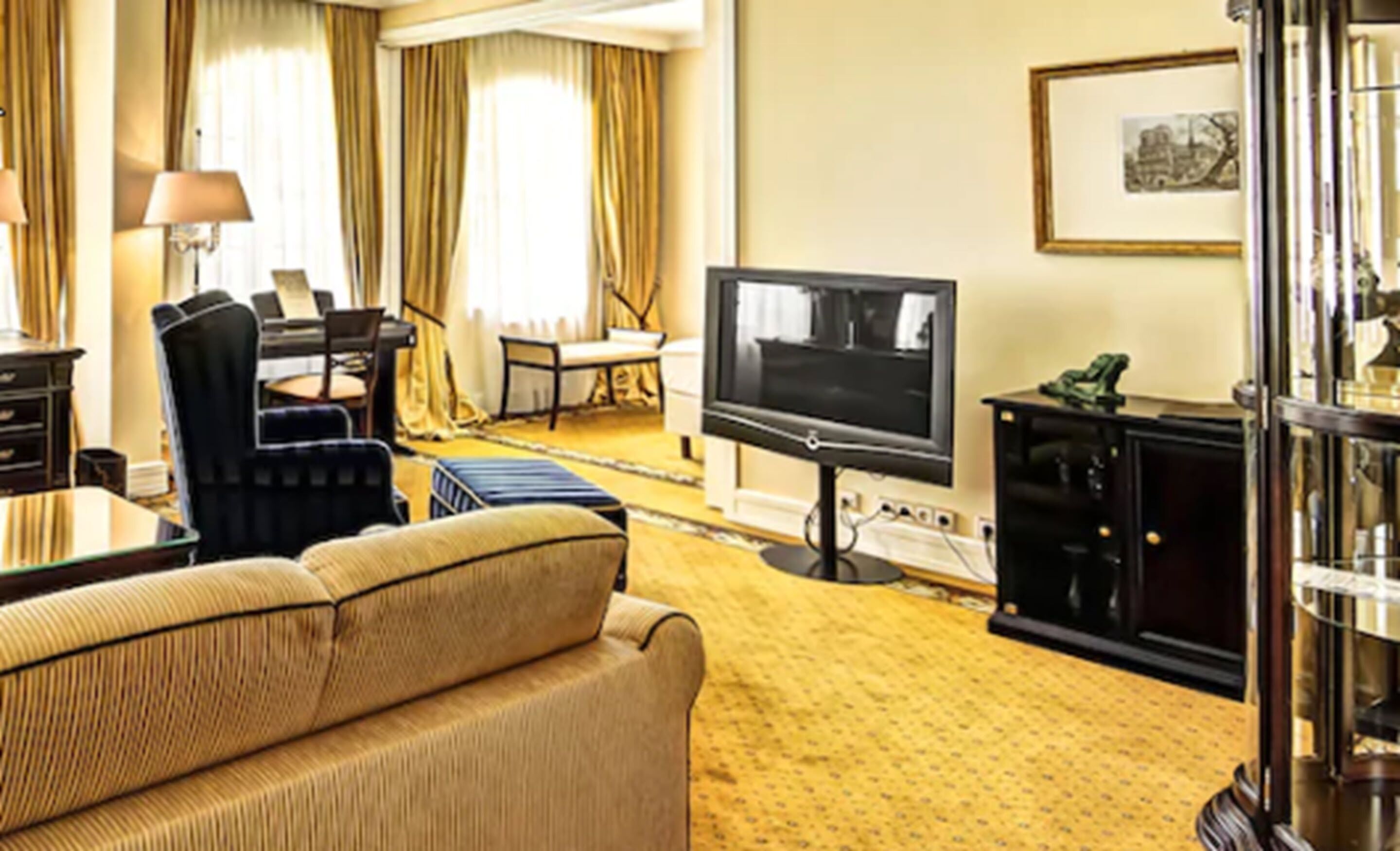 A hotel room with a sofa, a television, a desk, and a chair.