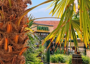 A hotel entrance with a sign, surrounded by lush greenery and a palm tree. - Hotel & Restaurant 5 Linden (Südharz)