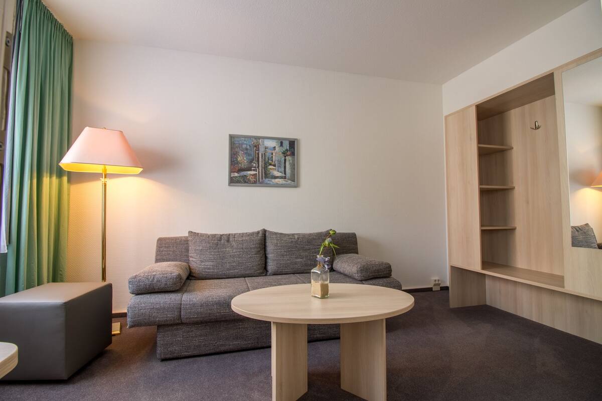 A modern living room with a grey sofa, a round wooden coffee table, a floor lamp, and a painting on the wall.