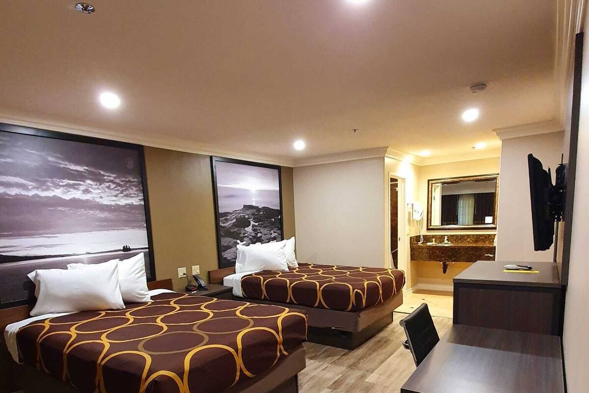 A hotel room with three beds, a desk, and a bathroom visible through an open door.
