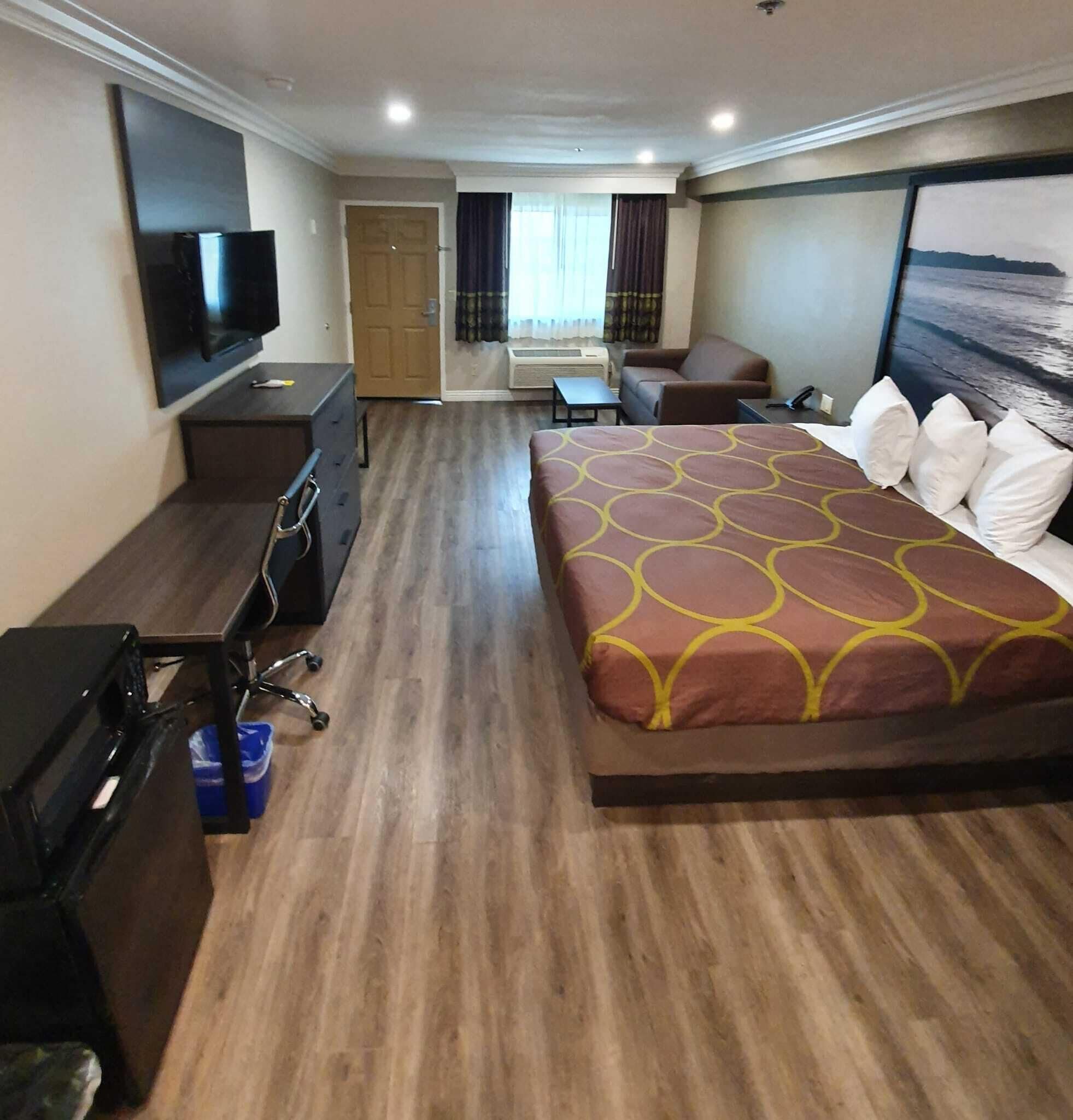 Une chambre d’hôtel avec un grand lit, un bureau, une chaise, une télévision et une fenêtre avec des rideaux.