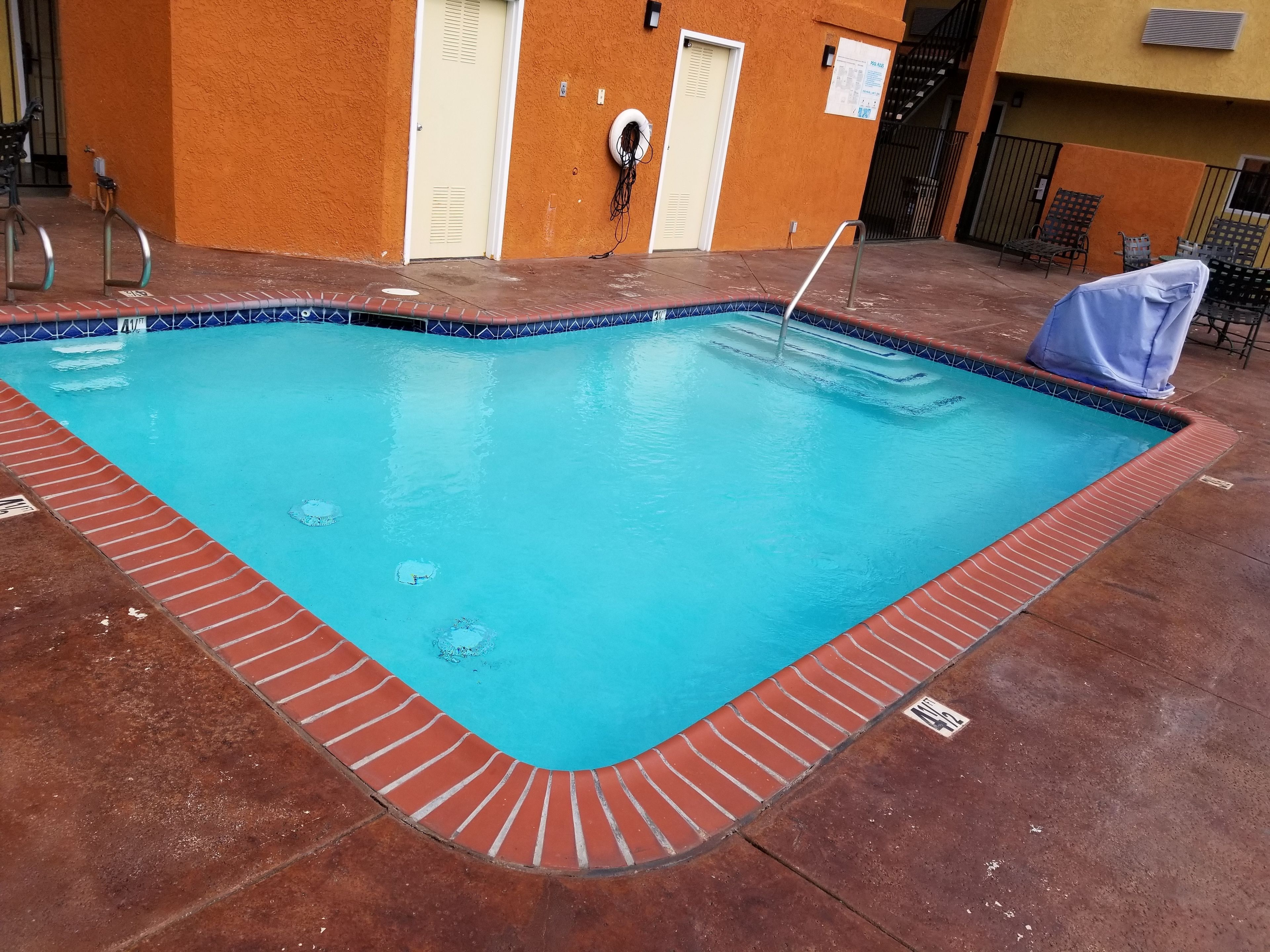 Piscina rectangular con interior azul y borde de ladrillo rojo.
