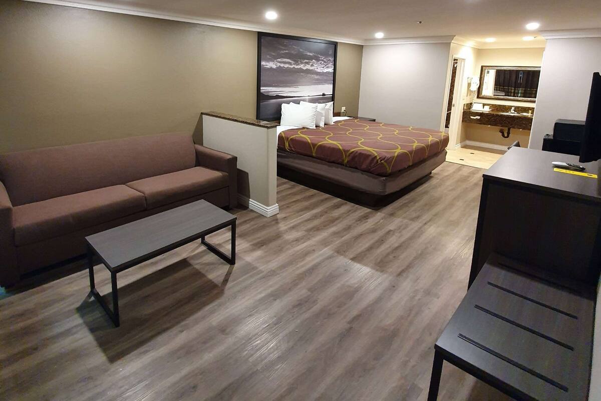 A hotel room with a bed, a sofa, a small table, a desk, and a bathroom visible through an open door.