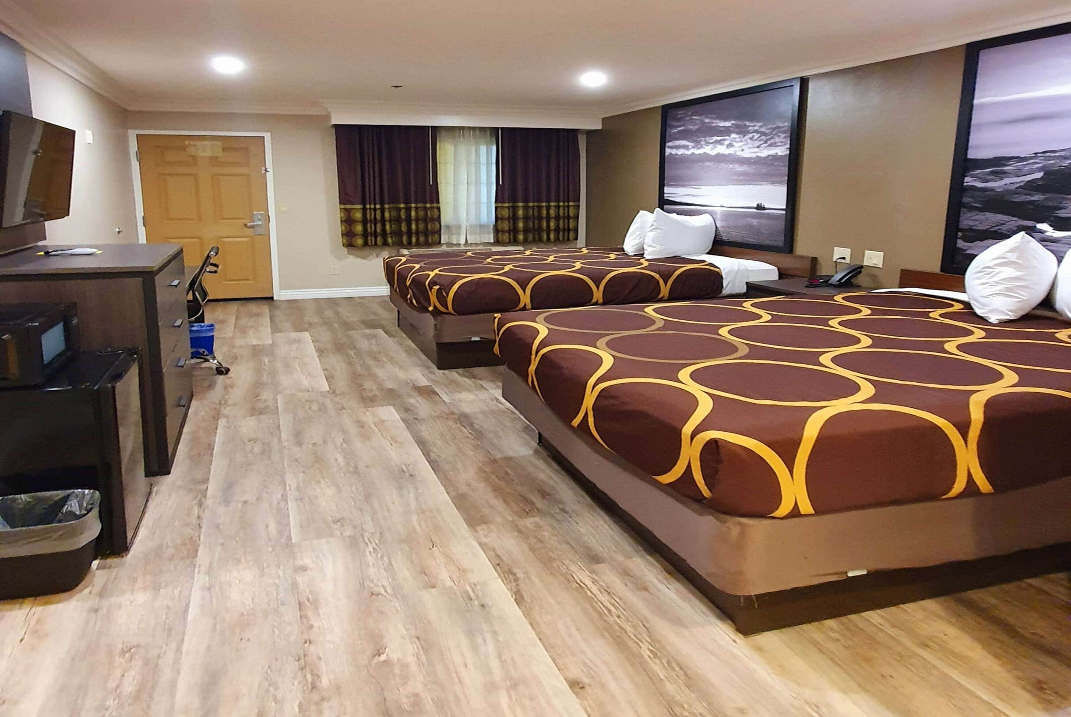A hotel room with three beds, a desk, and a TV.