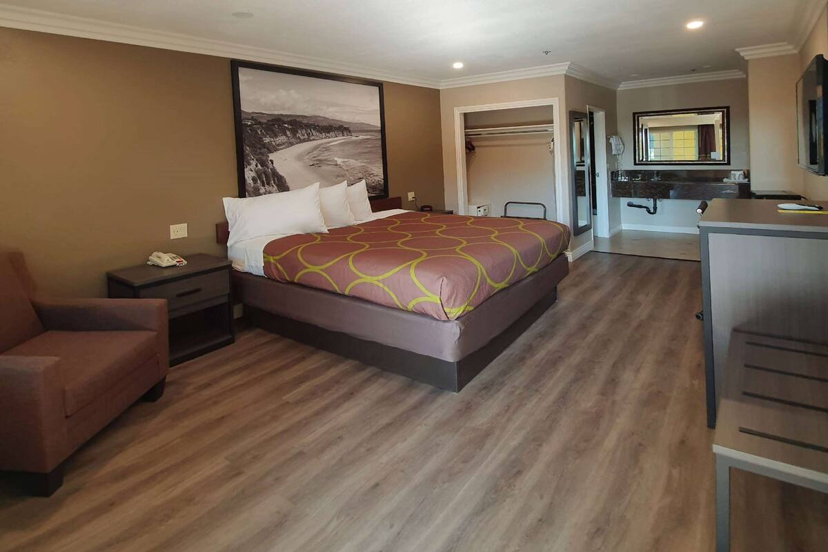 A hotel room with a large bed, a desk, a chair, and a wardrobe.