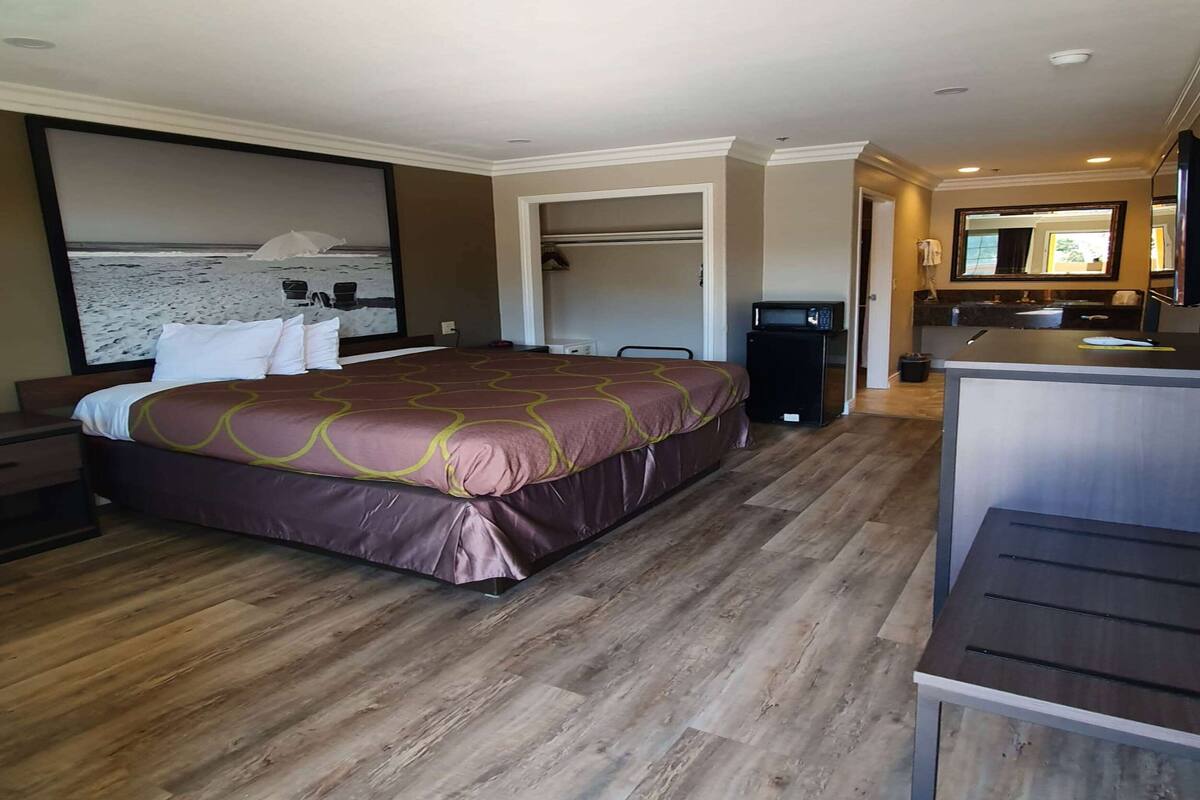 A hotel room with a large bed, a desk, a mirror, and a view of the beach.