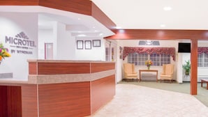 Un'area reception con una scrivania in legno, certificati incorniciati al muro, un angolo salotto con due poltrone, un tavolino con un vaso di fiori e un televisore appeso al muro.