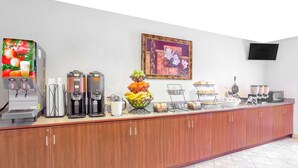 Un lungo bancone con macchine da caffè, una ciotola di frutta e un espositore per il pane.