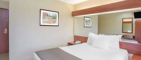 A hotel room with a large bed, a bedside table with a phone, a mirror, and two framed pictures on the wall.