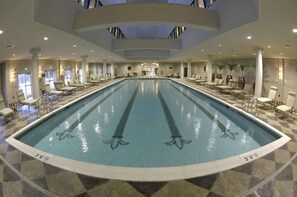 An indoor swimming pool with clear lane markings, surrounded by lounge chairs and tables, and a high ceiling with skylights. - West Baden Springs Hotel (West Baden Springs)