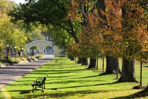 A park pathway lined with trees and benches, leading to a building with an arched entrance. - West Baden Springs Hotel (West Baden Springs)
