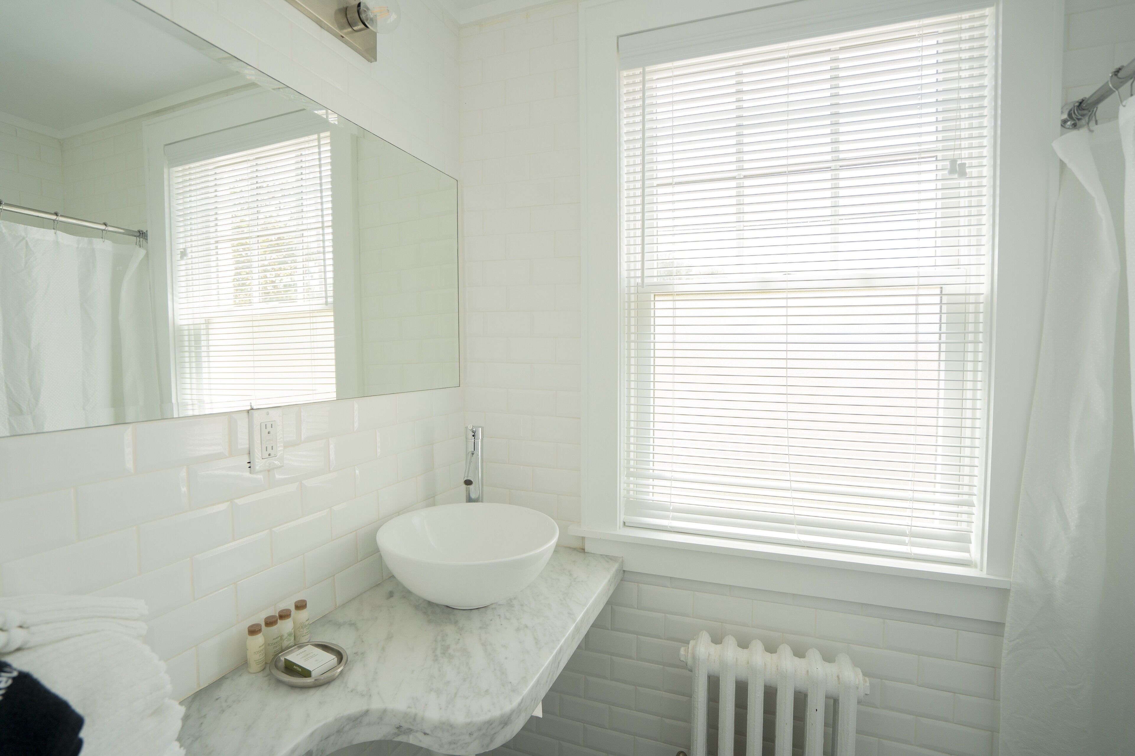 A bathroom with a white sink, a mirror, and a window with blinds.