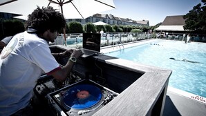 Een DJ-installatie met een laptop en draaitafel bij een zwembad.
