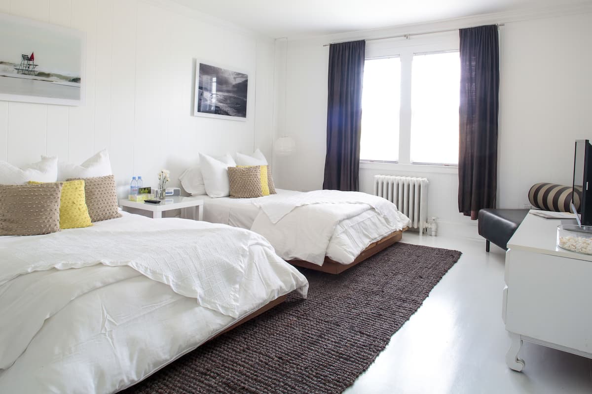 Une chambre d’hôtel avec deux lits, un bureau, une chaise, un radiateur et une fenêtre avec des rideaux.