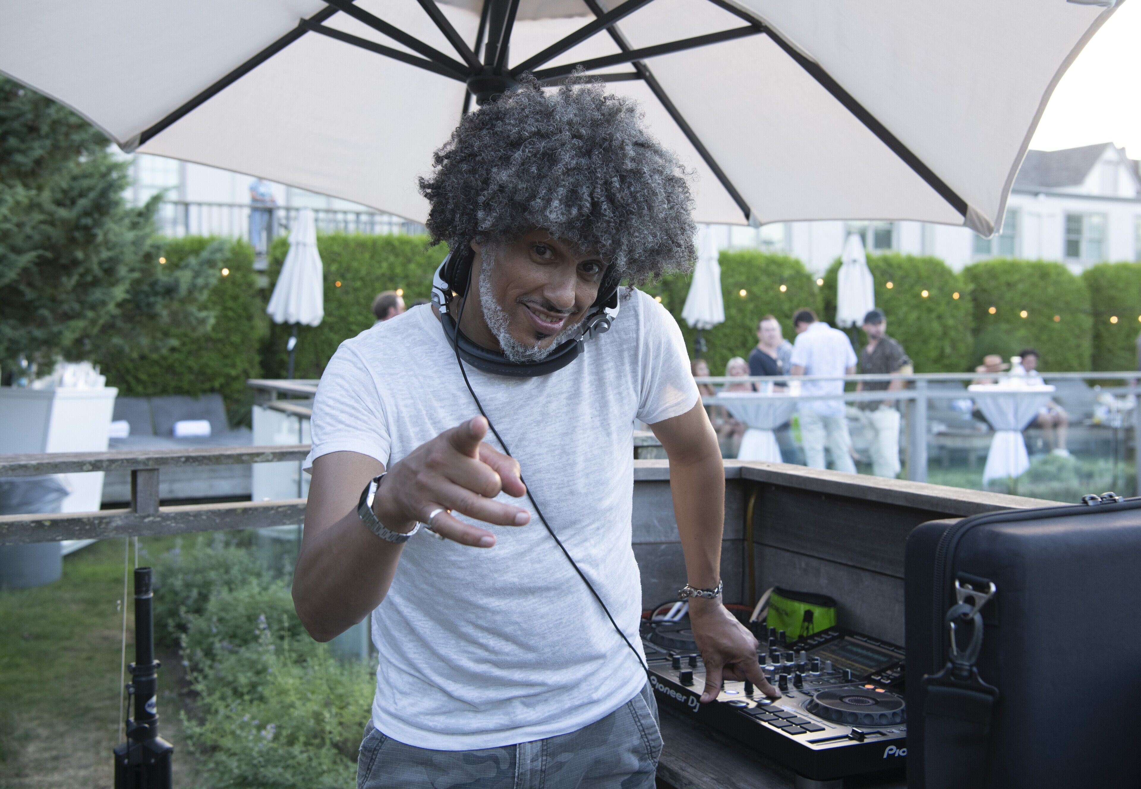 Une personne se tient près d’une table de mixage et de platines, sous un grand parapluie.
