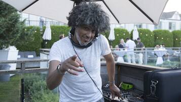 Une personne se tient près d’une table de mixage et de platines, sous un grand parapluie.