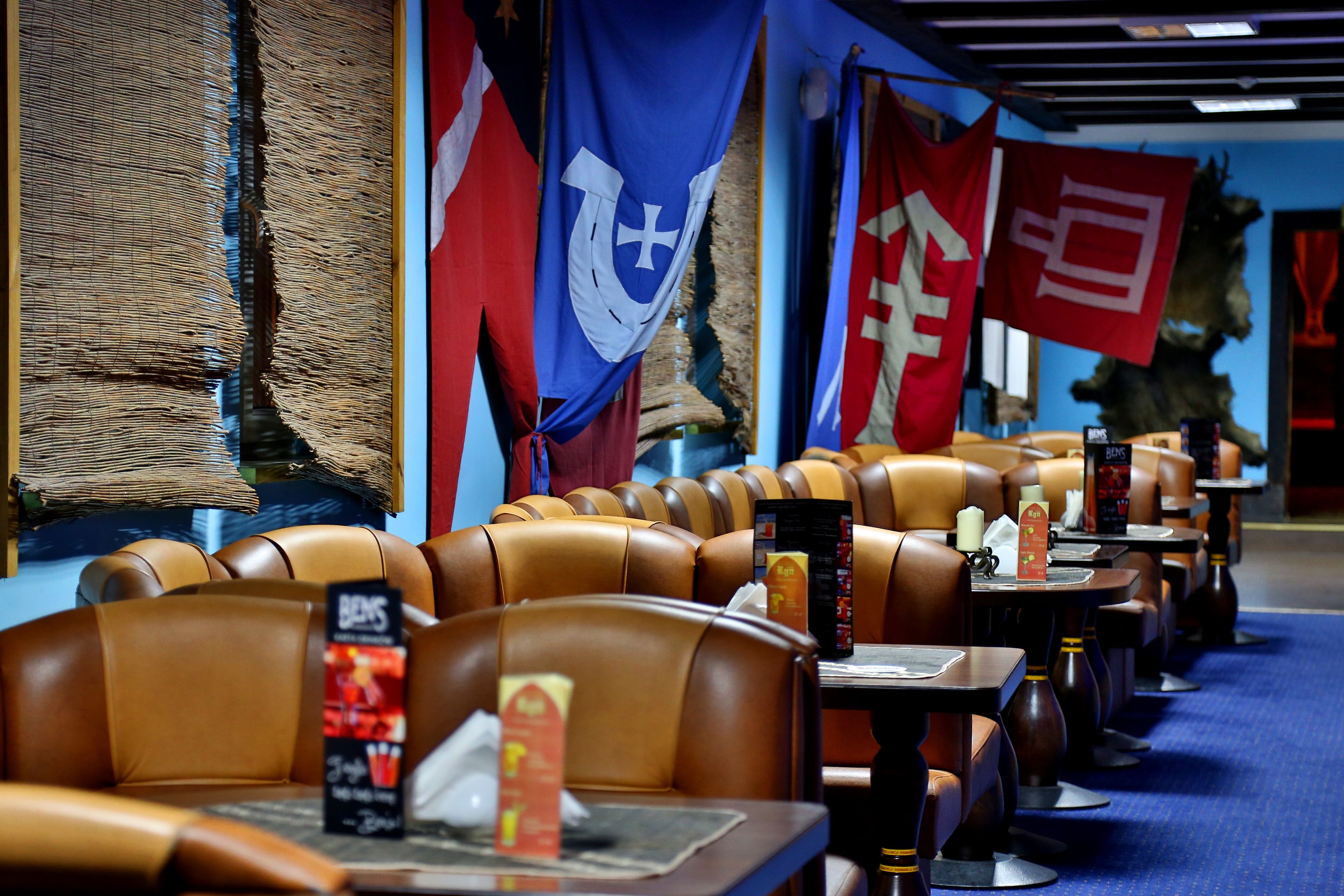 A restaurant with leather booths and tables, flags on the wall, and a blue carpet.
