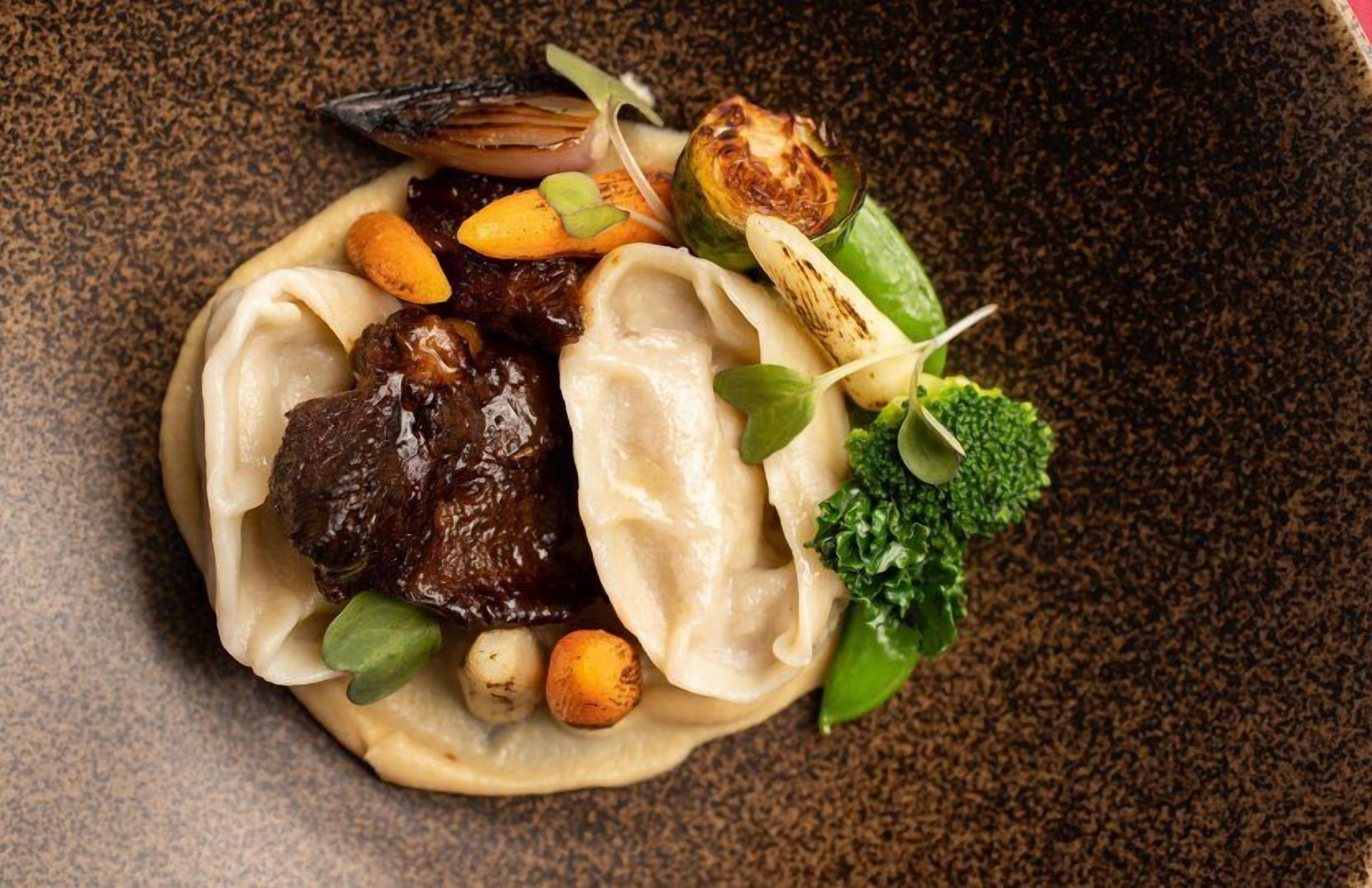 A dish with dumplings, meat, vegetables, and a garnish.