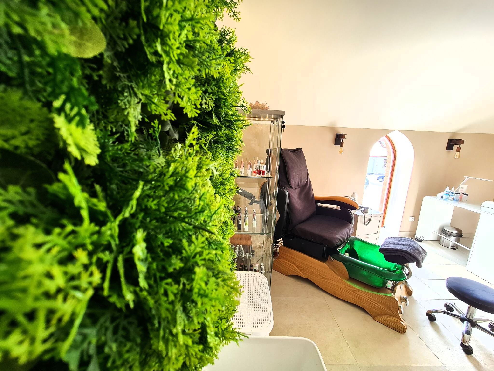 A spa room with a green wall, a massage chair, a small table with bottles, and a window with a view of the street.