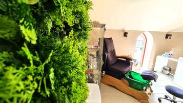 Ein Spa-Raum mit grüner Wand, einem Massagesessel, einem kleinen Tisch mit Flaschen und einem Fenster mit Blick auf die Straße.