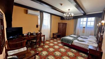 A hotel room with a large bed, a desk with a television, a wardrobe, and a carpet with a traditional pattern.