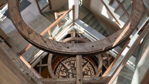Una escalera de caracol con barandillas de madera y un ventanal circular de vitrales en la parte superior.