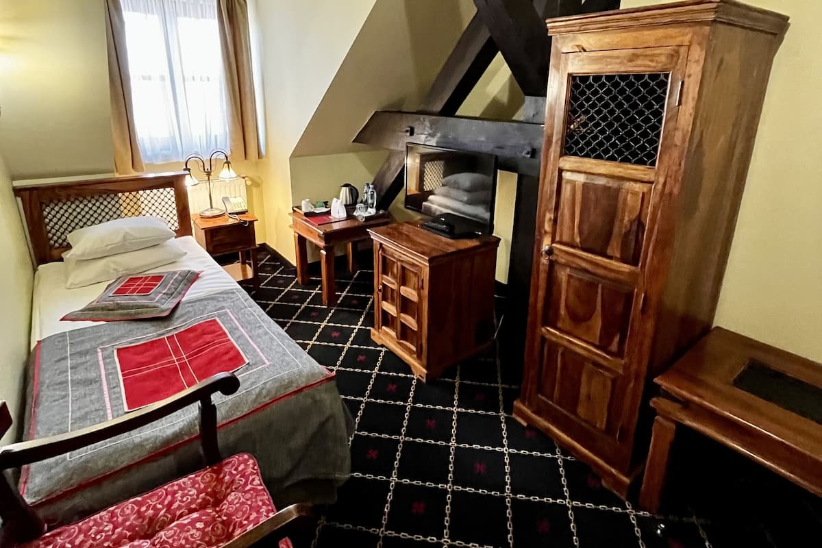 A bedroom with a bed, a wooden cabinet, a small table, and a chair.