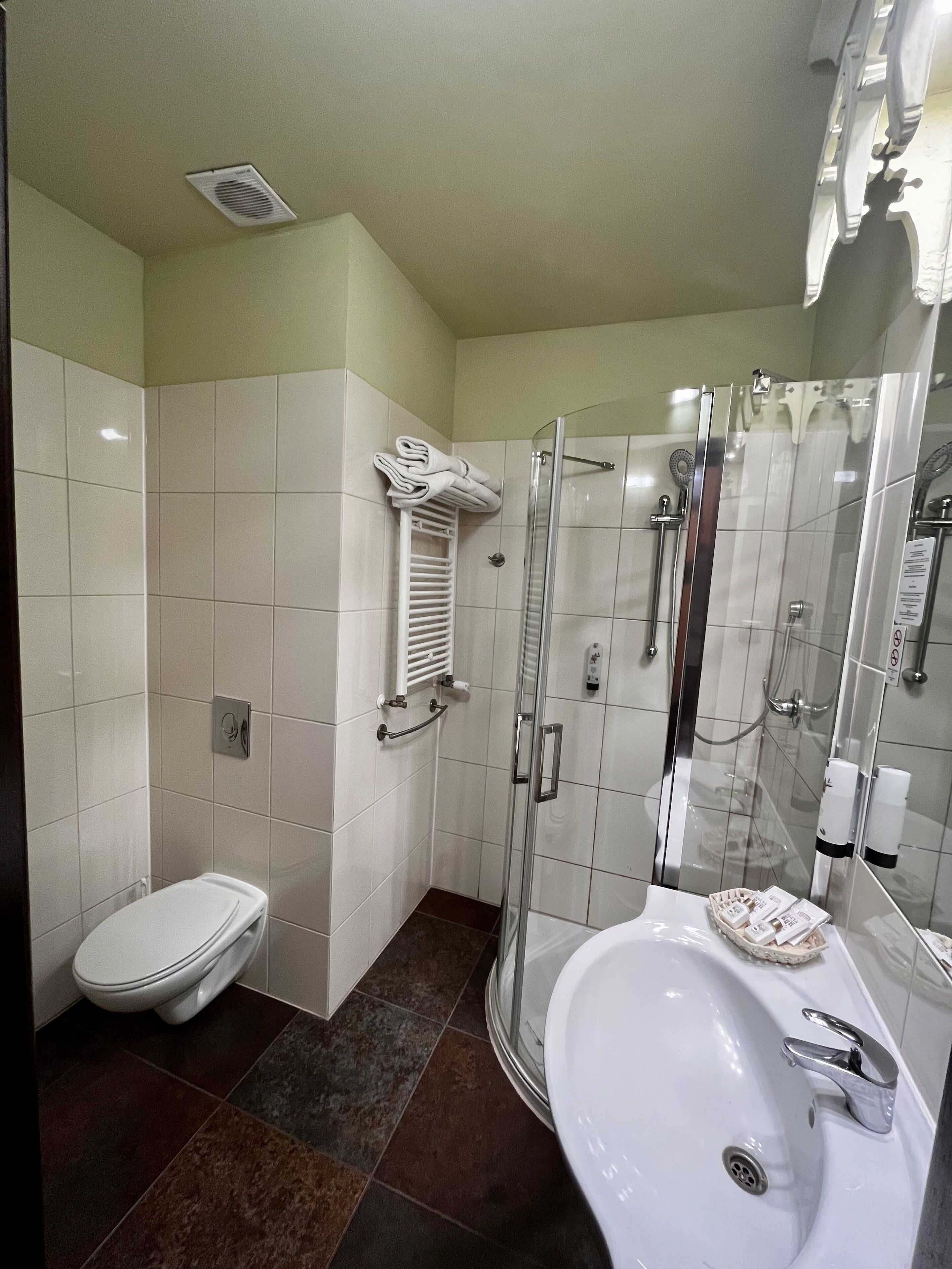 Ein modernes Badezimmer mit einer Glaskabine zur Dusche, einem weißen Waschbecken mit Chromarmatur und einer Toilette.