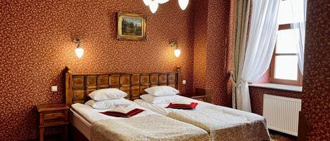 Una cama doble con dos almohadas, una mesita de noche, un cuadro enmarcado y una ventana con cortinas.