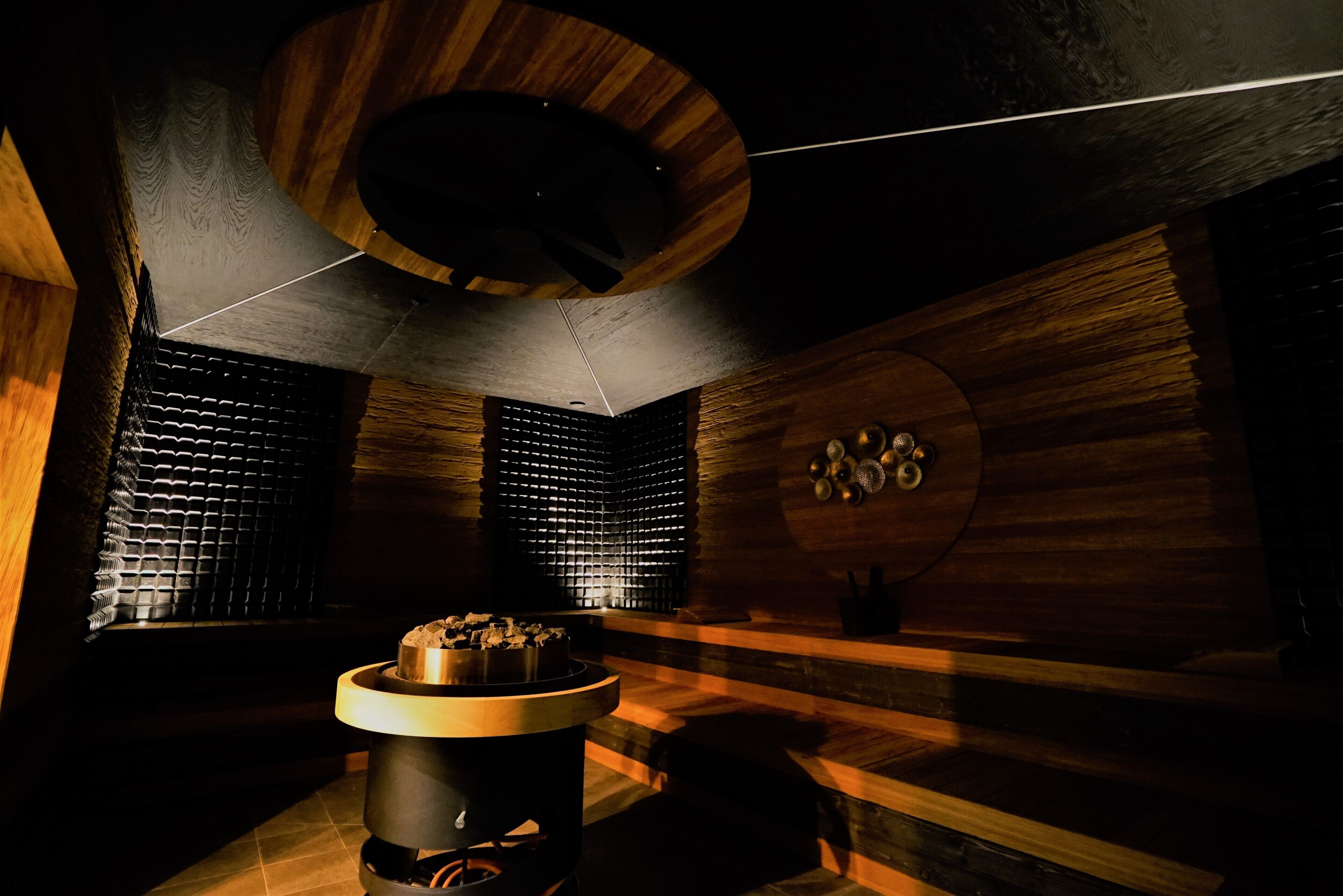 A sauna with wooden walls, a central heating unit, and a ceiling light fixture.