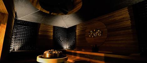 A sauna with wooden walls, a central heating unit, and a ceiling light fixture.