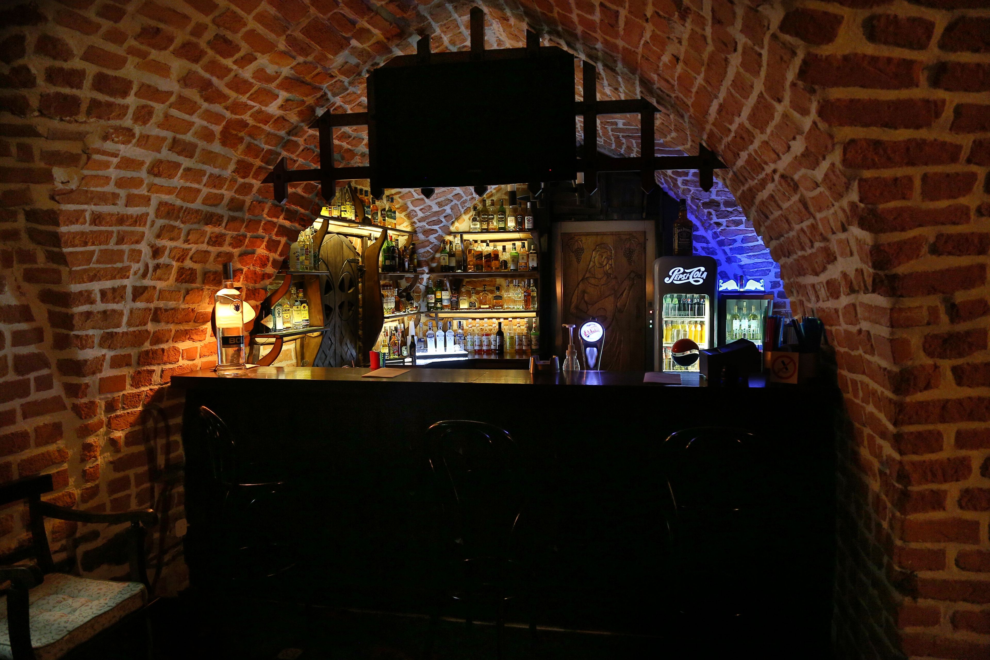 A bar area with brick walls, a counter, and a variety of bottles and glasses.