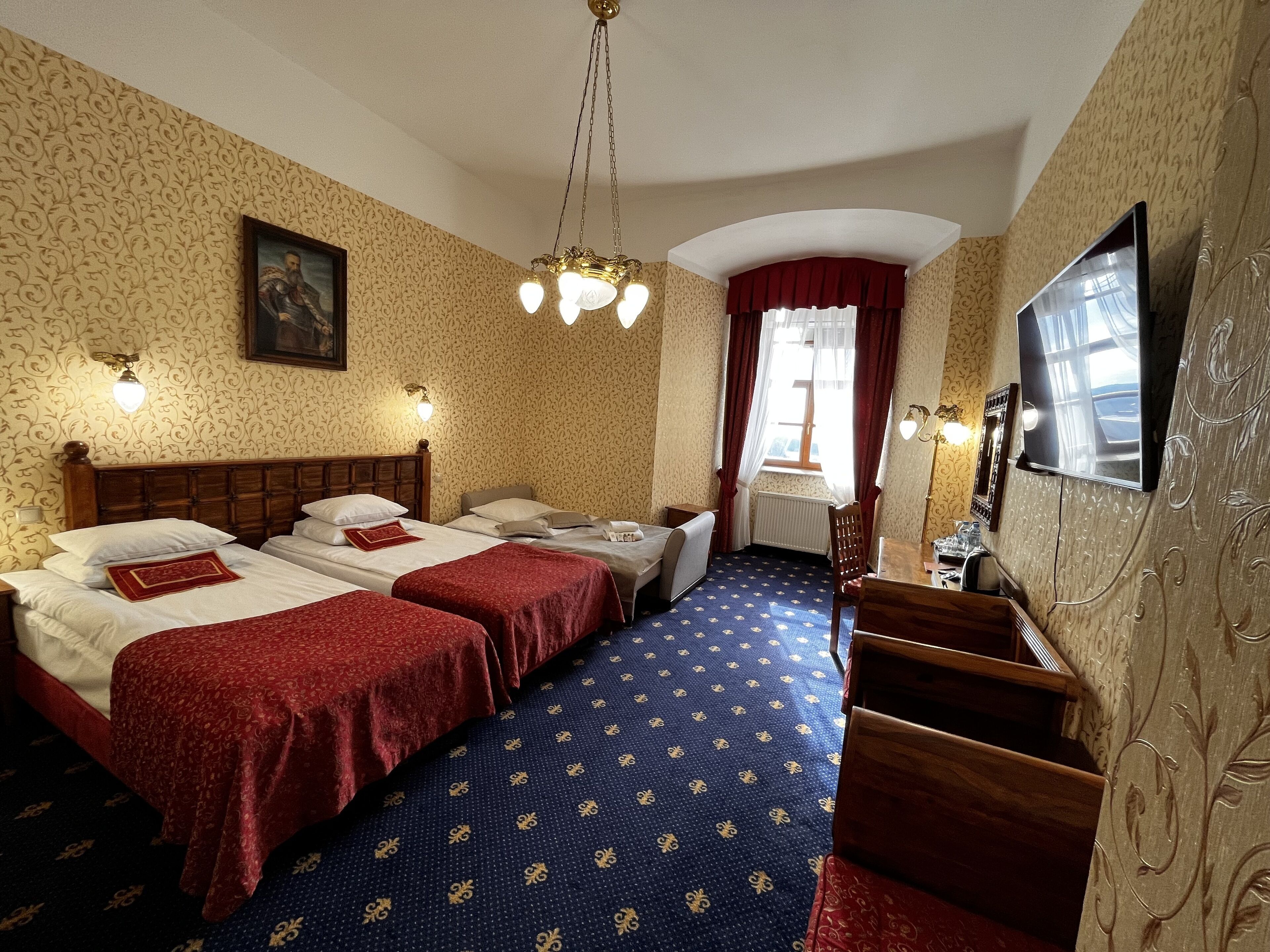 A hotel room with two beds, a desk, a TV, and a patterned carpet.