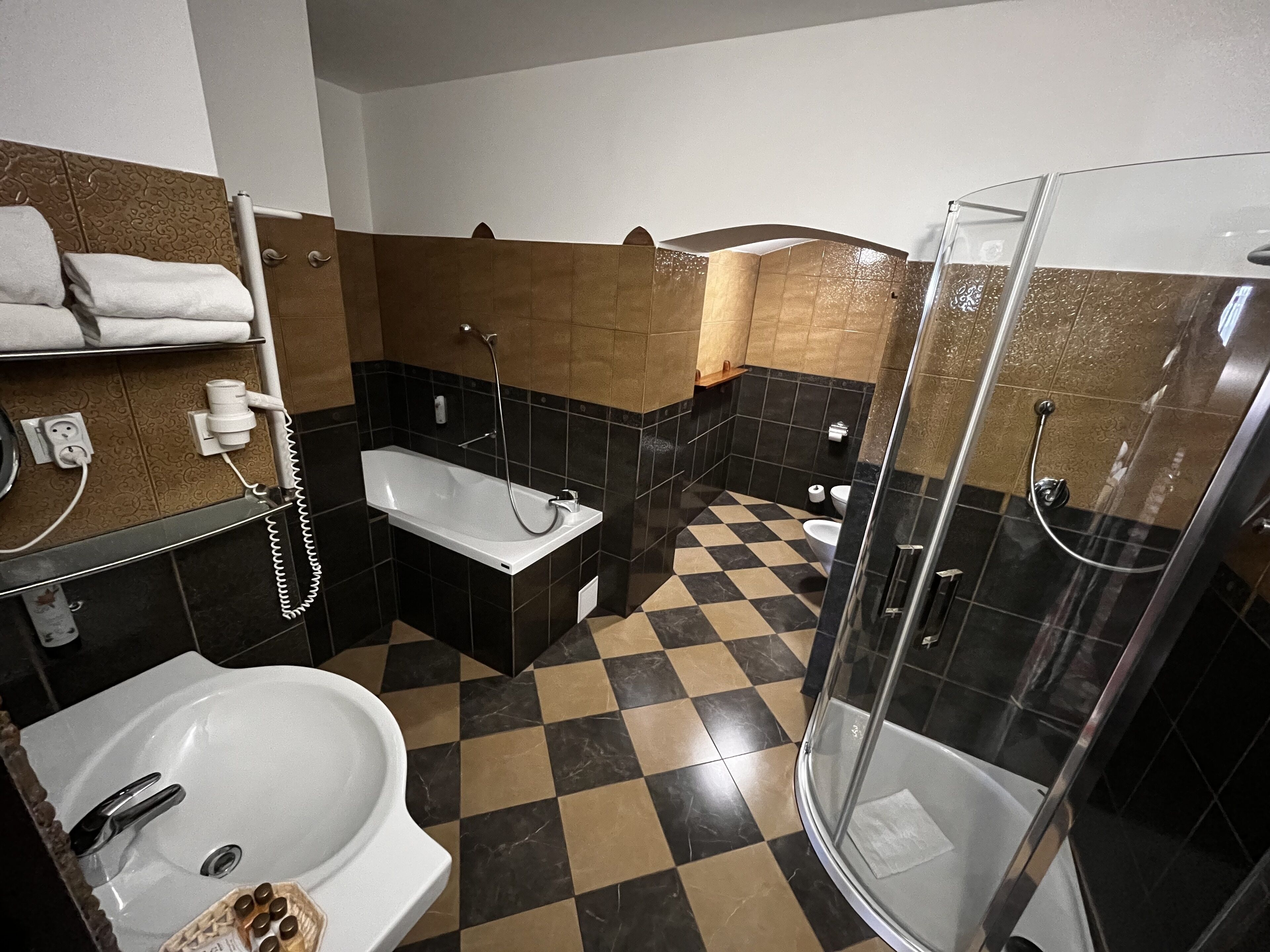 Une salle de bain avec un carrelage à motifs géométriques, un lavabo blanc, une baignoire, une douche et des toilettes.