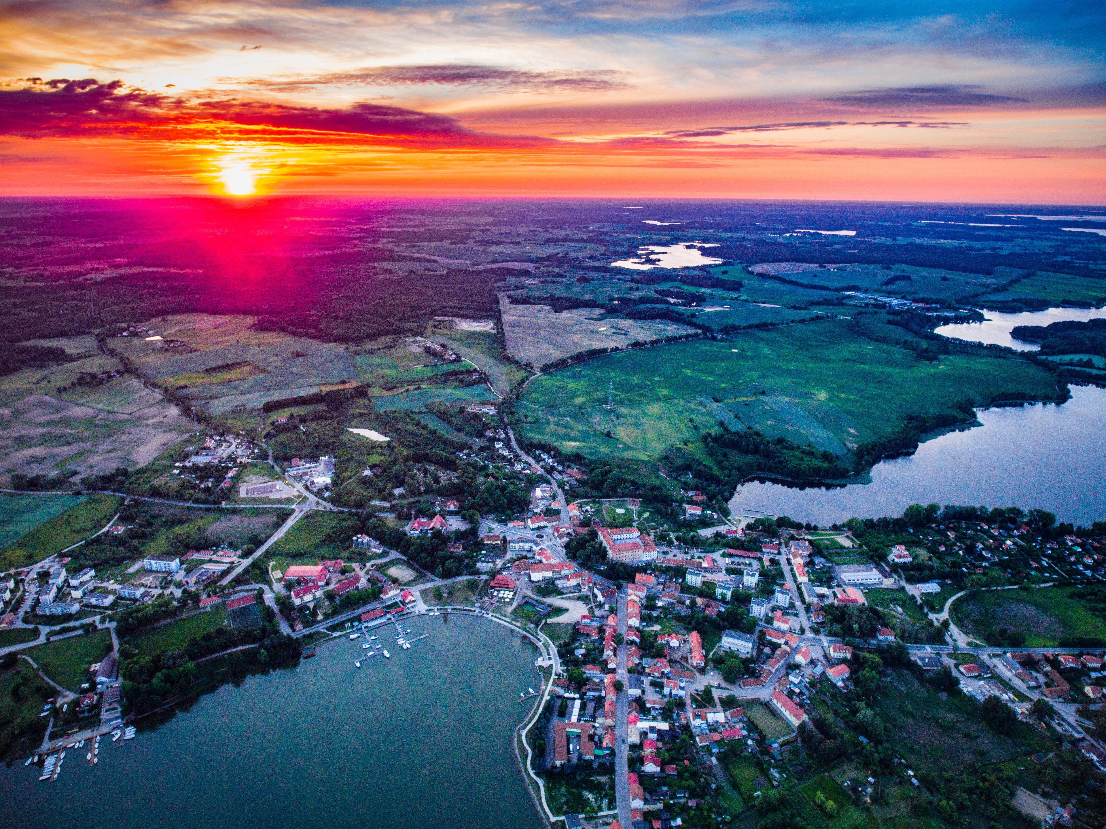 Une vue aérienne d’une ville bordée d’un lac, entourée de champs, avec un coucher de soleil en arrière-plan.