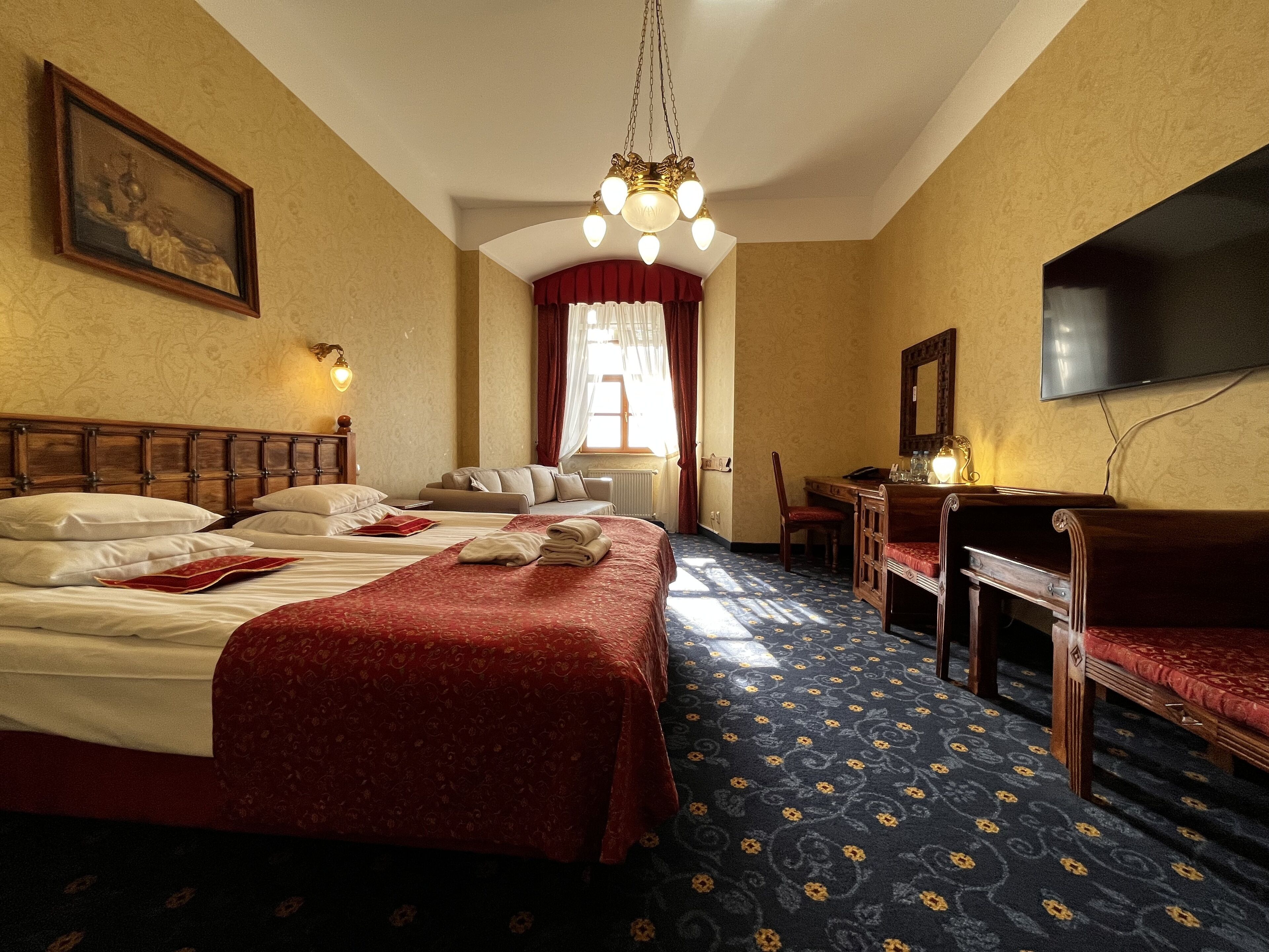 Une chambre d’hôtel avec un grand lit, un bureau, une chaise, une télévision et un lustre.
