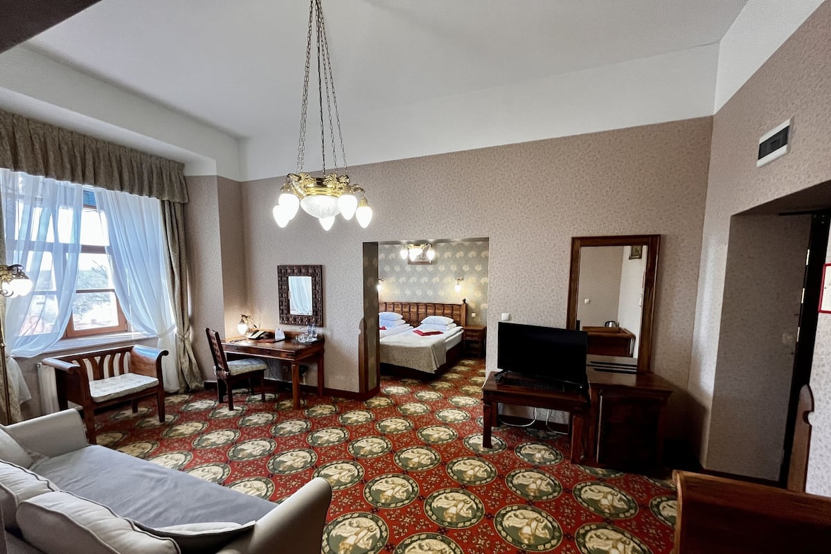 A hotel room with a bed, a desk with a chair, a television, and a sofa.