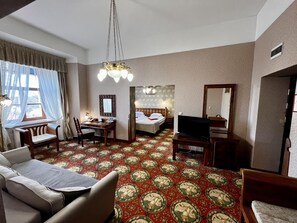 A hotel room with a bed, a desk with a chair, a television, and a sofa.