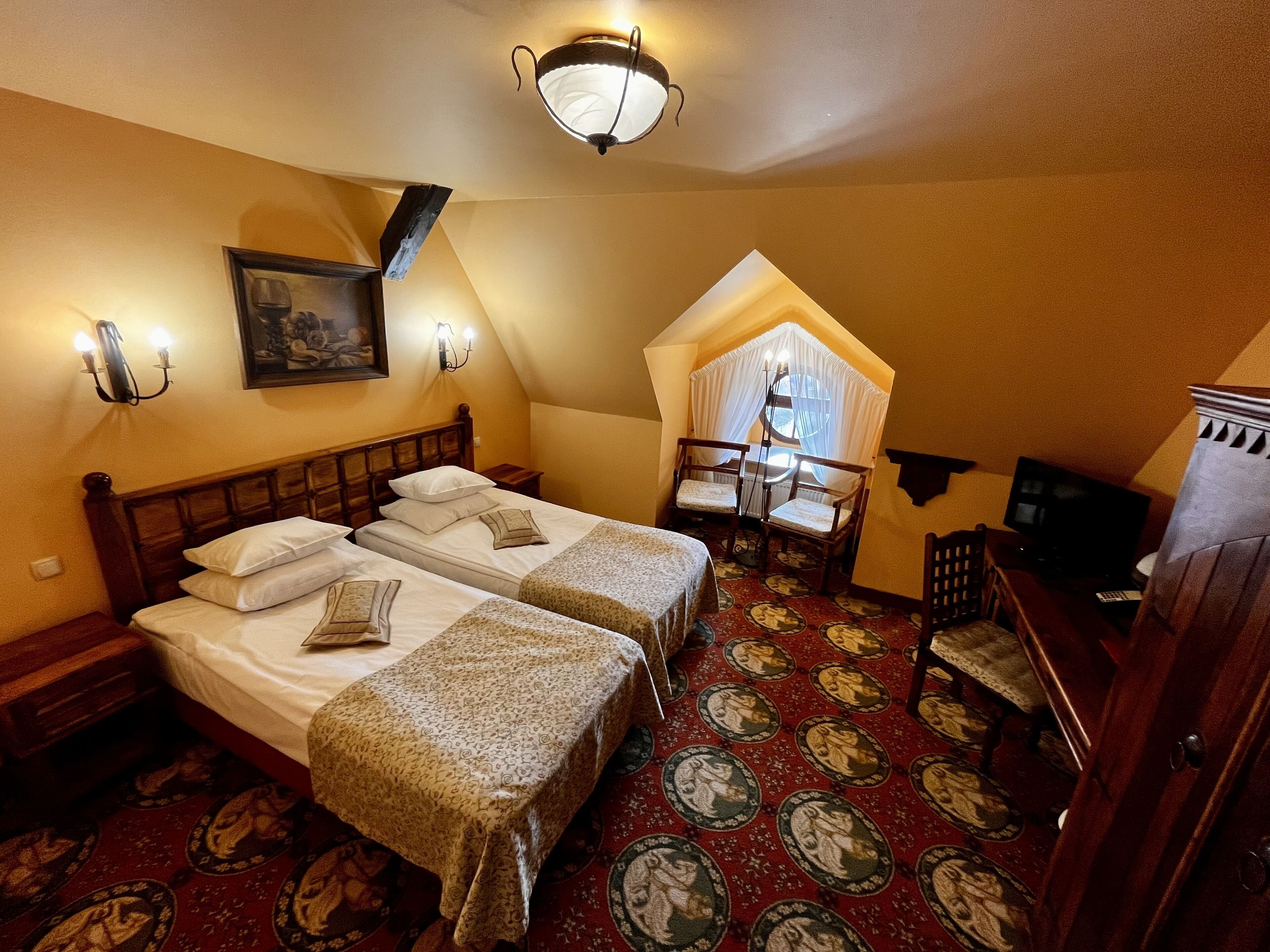 A room with two beds, a desk, a chair, a television, and a decorative ceiling light.