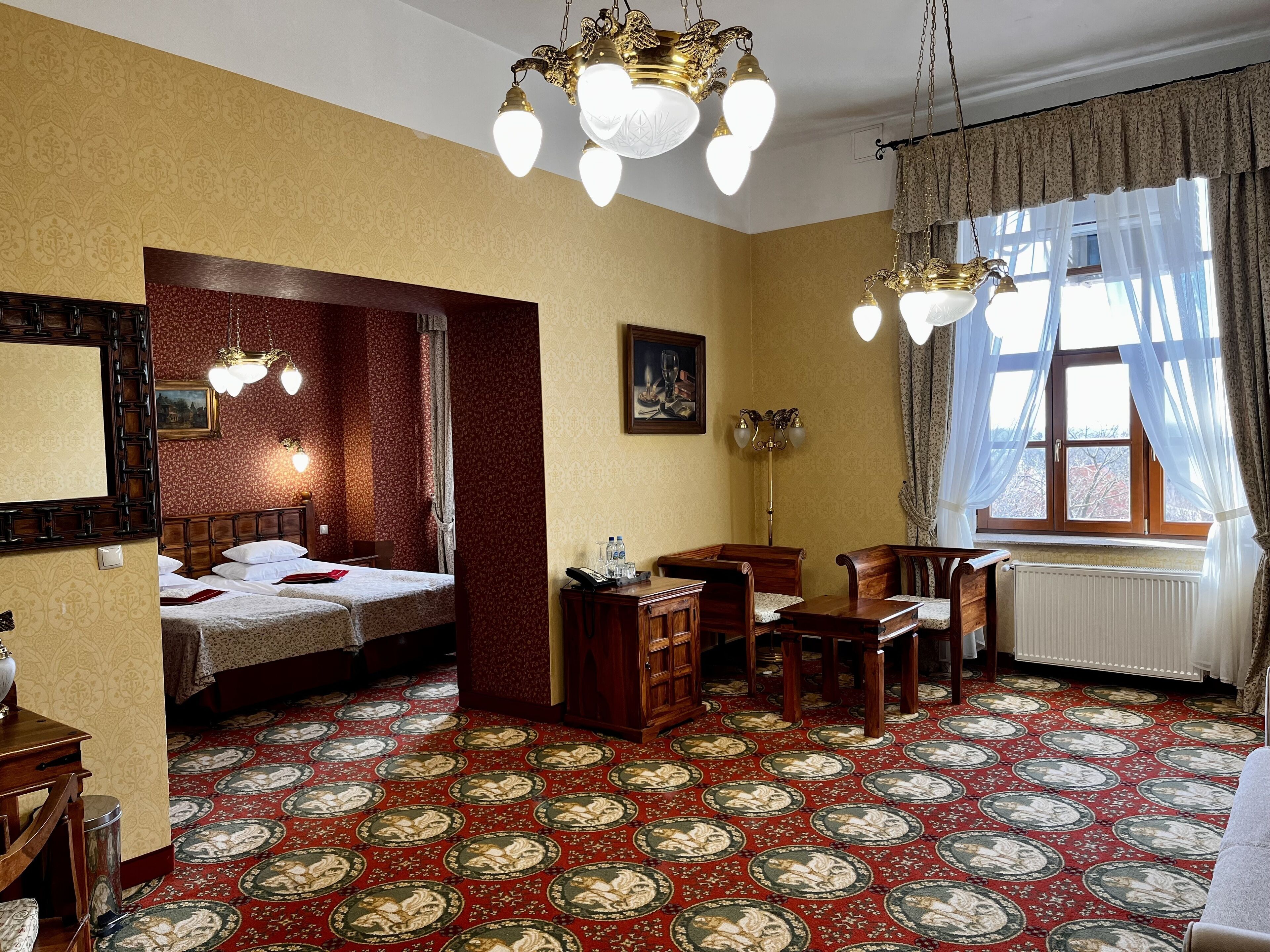 A hotel room with two beds, a dining area, and a large window with curtains.