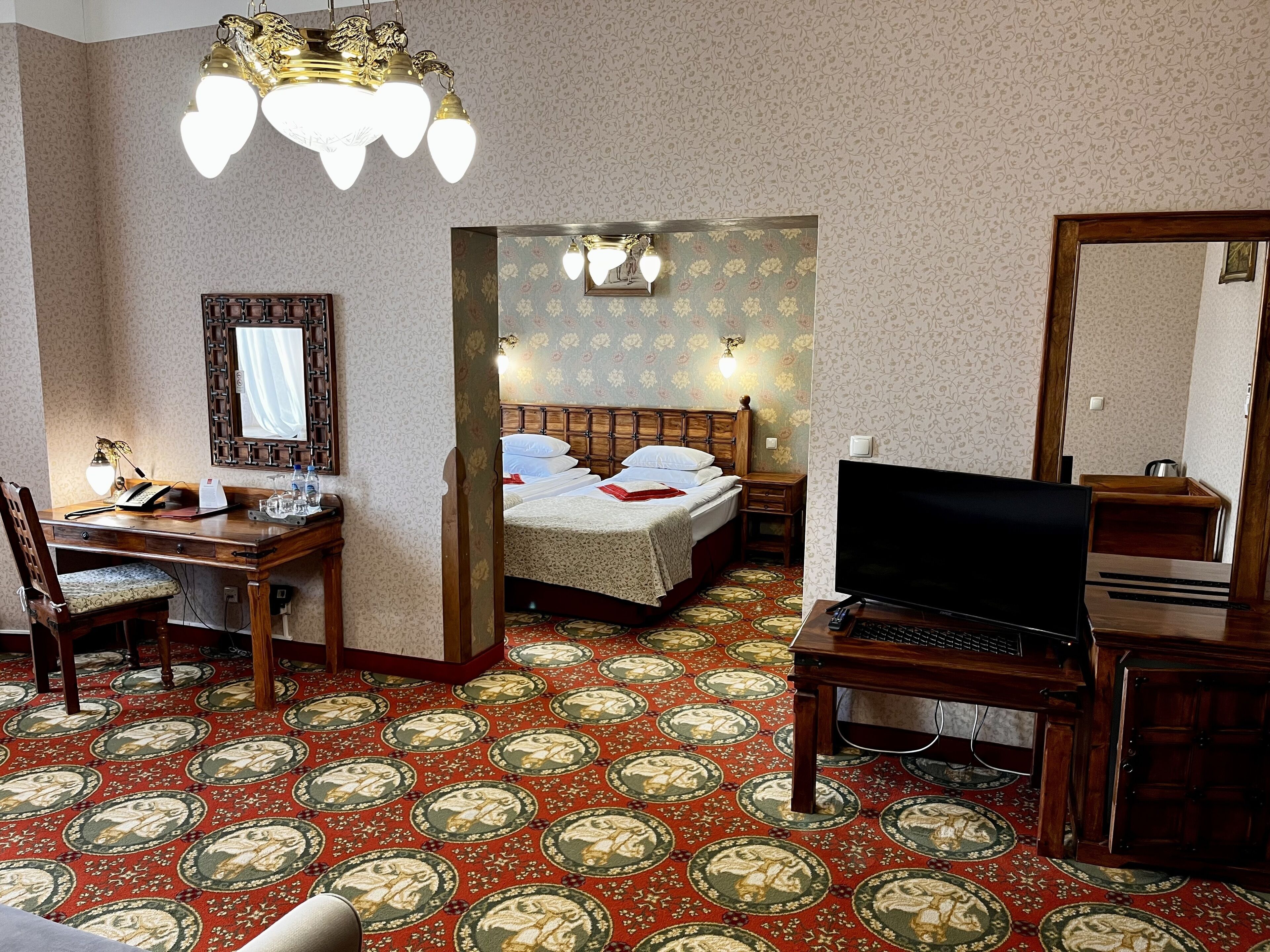A hotel room with a bed, desk, chair, television, and a carpet with a circular pattern.