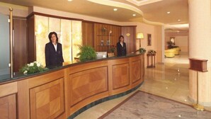 A reception area with a curved wooden reception desk, two receptionists, and a well-lit interior with a marble floor. - Parco Serrone (Corato)