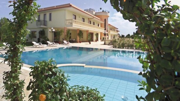 A poolside view of a hotel with a large pool, lounge chairs, and a building with balconies. - Parco Serrone (Corato)