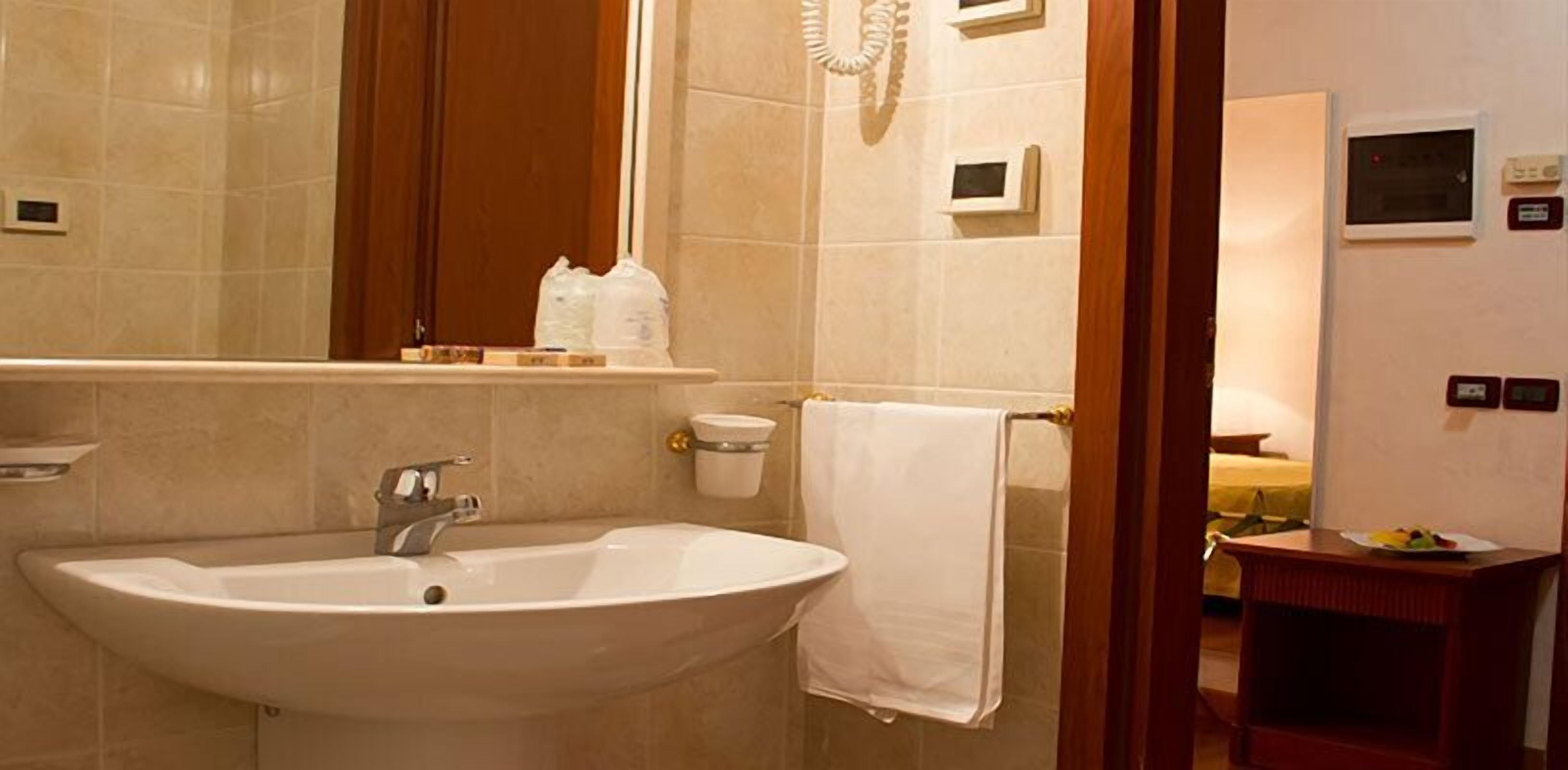 Un baño con lavamanos, espejo, toallero y un pequeño estante con artículos de aseo.
