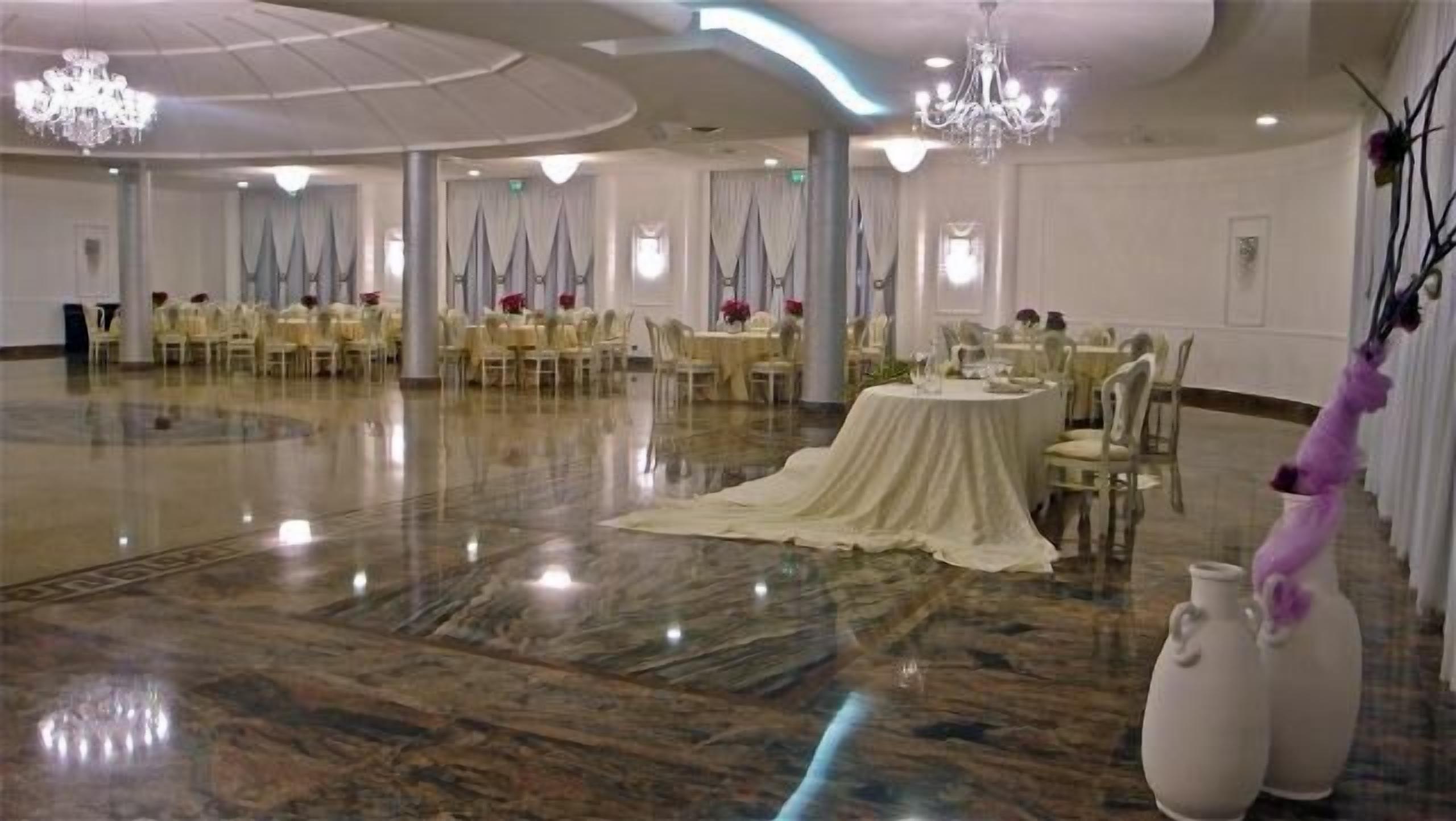 Un salón amplio con mesas y sillas redondas, candelabros y un piso de mármol pulido.