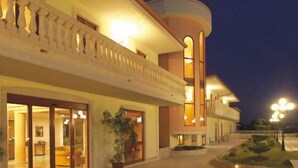 A hotel exterior at night with a spacious entrance, a covered walkway, and a well-lit building facade. - Parco Serrone (Corato)