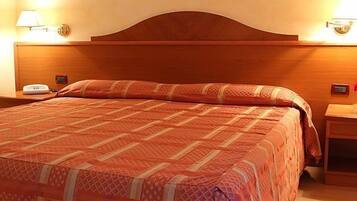 A hotel room with a wooden headboard, a patterned bedspread, a bedside table with a lamp, and a vase with flowers.