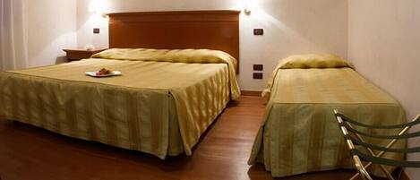 A hotel room with two beds, wooden flooring, and a nightstand with a lamp.
